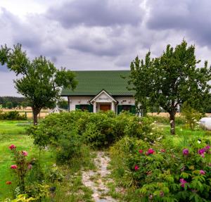a house with a green roof and trees and flowers at Biały Domek w Ogrodzie Różanym 