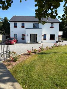a white house with a red car parked in front of it at Ashlee Lodge, Shanagarry P25K6R6 Near Ballymaloe Cookery School & Garryvoe Hotel in Shanagarry