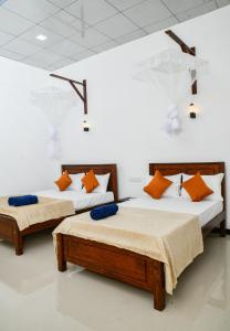 two beds in a white room with orange pillows at EverGreen Resort Udawalawe in Udawalawe