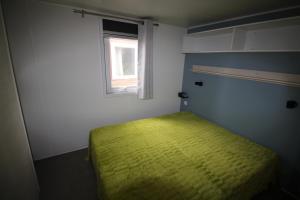 ein kleines Schlafzimmer mit einem grünen Bett und einem Fenster in der Unterkunft Land's Hause Bungalows par La Conciergerie Française Emplacement S6 in Pataias