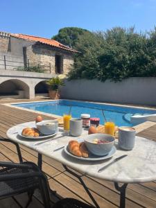 une table avec de la nourriture pour le petit-déjeuner et des boissons à côté d'une piscine dans l'établissement La Tuilerie du Bazalac, à La Celle-sous-Gouzon