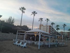 un gruppo di tavoli e sedie sulla spiaggia con palme di La Casa de Ely a Sant Carles de la Ràpita