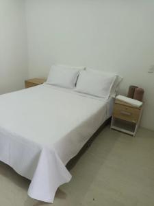 a white bed with white sheets and pillows and a night stand at Edificio Sierra Beach Resort Pozos Colorados vista y salida al mar in Santa Marta
