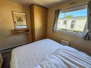 a small bedroom with a bed and a window at Great Caravan At Valley Farm Holiday Park, Essex Ref 46583V in Great Clacton