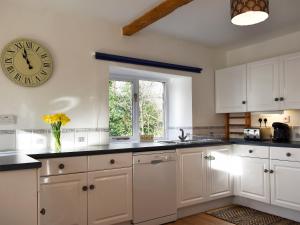 a kitchen with white cabinets and a clock on the wall at Grange Cottage in Winston