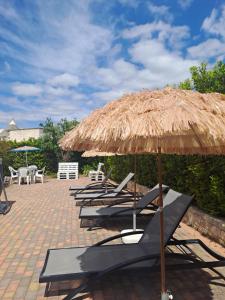 a row of lounge chairs under a straw umbrella at Trulli di Rosa in Locorotondo