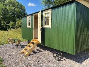 a green tiny house with a ladder and a table at Cosy Shepherd Hut in Kempsford