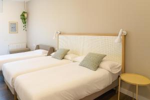 two beds in a room with white sheets and a table at Langre Homely Rooms in Galizano