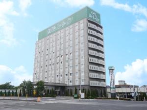 Un gran edificio blanco con un cartel verde. en Hotel Route-Inn Hirosaki Joto, en Hirosaki