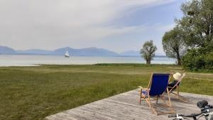two chairs on a dock with a sailboat in the water at Familiennest Vogelwuid in Seebruck