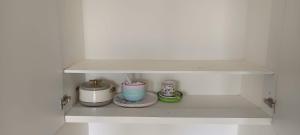 a shelf in a white kitchen with cups and plates at HimaViswa Farmstay in Hospet