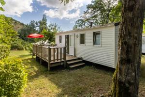 a tiny house with a deck and a red umbrella at Mobilhome Le Tilleul in Saint-Pompont