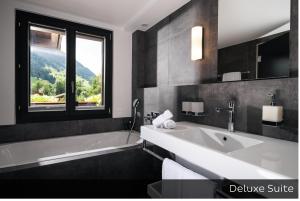 een badkamer met een bad, een wastafel en een raam bij Hotel Arc-en-ciel Gstaad in Gstaad