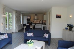 a living room with two blue couches and a kitchen at Dunopark Villa in Oostkapelle