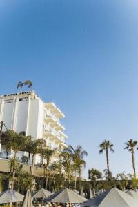 a large white building with palm trees and umbrellas at Demi Hotel in Sarandë