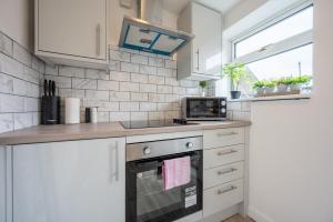 a kitchen with white cabinets and a stove at Silver Street by Tŷ SA in Troed-y-rhiw