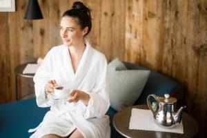 a woman in a robe holding a cup of coffee at Mirabell Dolomites Hotel - Luxury Ayurveda & Spa in Valdaora