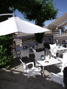 un grupo de mesas y sillas con una sombrilla blanca en Hostal Salones Victoria en Santa Marina del Rey