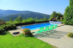 a swimming pool with green chairs in front of it at Chata Jezevec in Hojsova Stráž