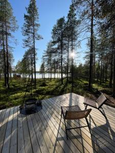 two chairs and a swing on a deck with trees at LaplandLiv Glampingtent with private sauna at the lake! in Mellanström