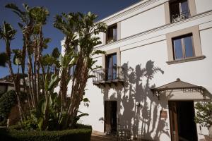a white building with a balcony and palm trees at Villa Dei Melograni Boutique Hotel in Cefalù