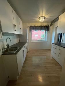 une cuisine avec des armoires blanches, un évier et une fenêtre dans l'établissement The Urban Escape Walk to Train, Bus & City Center, à Narvik