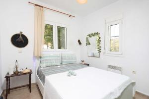 a white bedroom with a bed and two windows at Η Μουριά, The Mouria House in Pefkochori