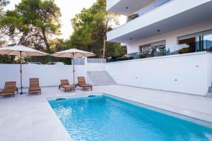 a swimming pool with chairs and umbrellas next to a house at Villa Bajlo in Ždrelac