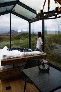 Panorama Glass Lodge SOUTH في هيلاّ: امرأة تقف في غرفة بسرير وطاولة +20 صورة
