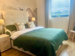 a bedroom with a bed with a green comforter and a window at Spacious 3BR City Centre Apartment Free Parking in Liverpool