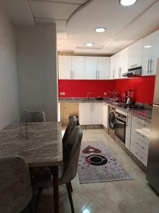 a kitchen with a table with chairs and red cabinets at Appartement Deluxe à côté de souq elhad in Agadir