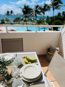 un tavolo con piatti e banane su un balcone di Appartement vue panoramique mer et piscine a Sainte-Anne