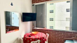 ein Raum mit einem Tisch und einem Fernseher an der Wand in der Unterkunft Apartamento Pé na Areia - Praia Grande in Praia Grande