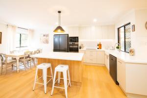 a kitchen with white cabinets and a kitchen island with stools at Miva Maison in Maleny