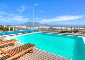 a swimming pool with benches and the ocean in the background at El Mufasa beachfront apartment with stunning views in Cape Town