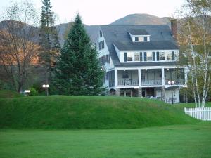 uma grande casa branca no topo de uma colina verde em Franconia Inn em Franconia