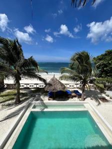 a pool on the beach with palm trees and the ocean at Amani Beach Villa- Bwejuu in Bwejuu