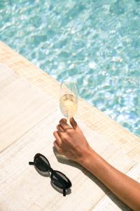 a person holding a wine glass next to a swimming pool at Zahara Beach & Spa by QHotels - Adults Recommended in Zahara de los Atunes
