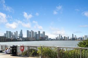 a group of people sitting next to the water with a city at Luxury 2 BR Riverview Ensuite Flat in Greenwich Near O2&Excel in London
