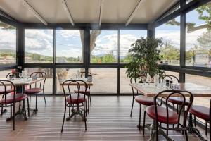 a room with tables and chairs and large windows at Hotel Restaurant Le Castel Fleuri in Carnoules
