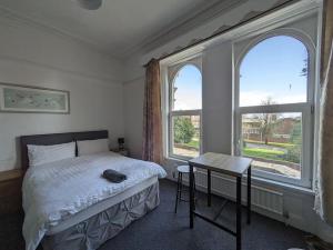 a bedroom with a bed and a table and two windows at Ensuite triple room by Swansea University Hospital v in Swansea