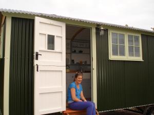 a woman sitting in the doorway of a green shed at Apple Tree Shepherd's Huts - Blackberry Hut in Saint Endellion