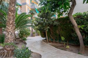 a walkway through a garden with palm trees and a building at Via Aurelia 17 Cozy Apartment in Salou