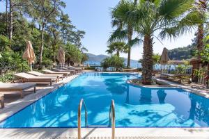 a pool with chaise lounge chairs and palm trees at Baga Hotel in Akyaka