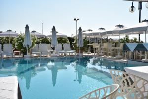 ein großer Pool mit weißen Stühlen und Sonnenschirmen in der Unterkunft Hotel Oxford in Lido di Jesolo