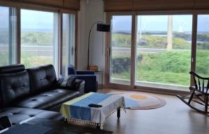 a living room with a leather couch and large windows at Jeju Noeul Bori Pension in Jeju +54 photos