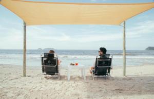 two people sitting in chairs under a tent on the beach at Ilha do Mel Lodges in Ilha do Mel