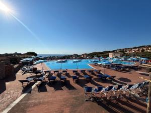ein Pool mit Stühlen und Sonnenschirmen neben dem Meer in der Unterkunft Calarossa Sardinia Apartments in Isola Rossa