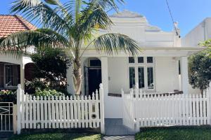 una cerca blanca frente a una casa blanca con una palmera en Marvelous Manly Home moments from the Beach - NEW, en Sídney