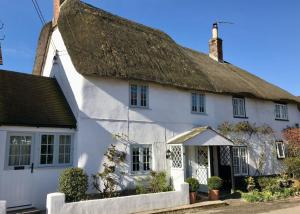 a white cottage with a thatched roof at Tudor Rose Cottage in Stourpaine